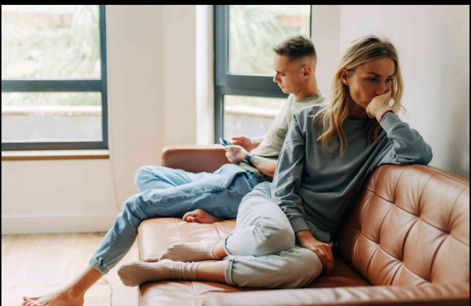 Emotionally exhausted couple sitting apart in quiet living room, illustrating burnout in relationships and emotional distance
